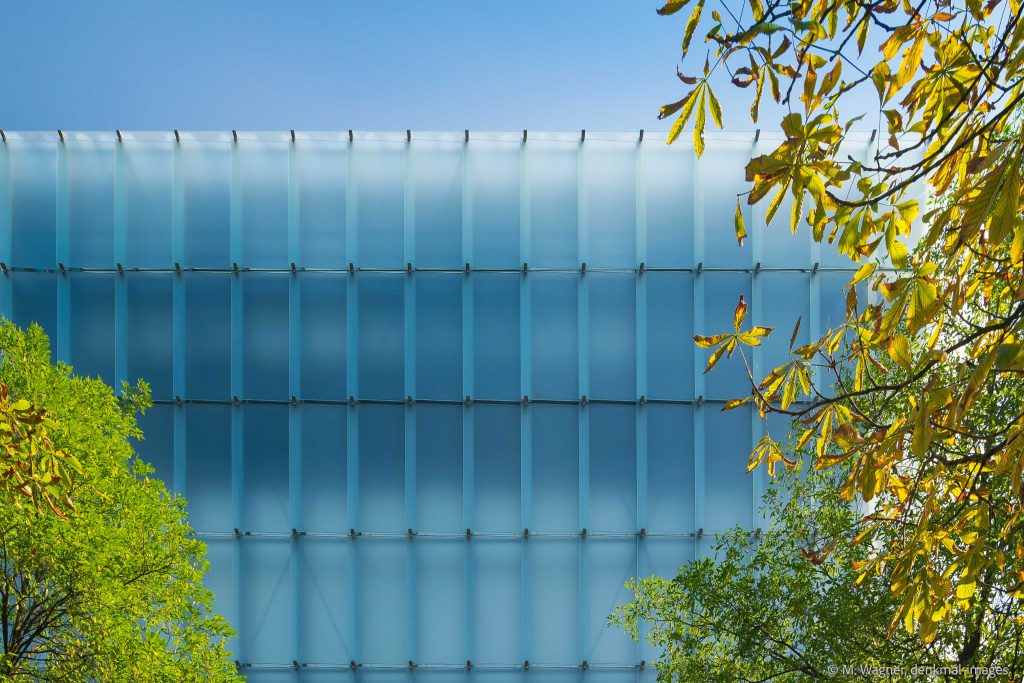 blaeuliche Fassade Kunsthaus mit vorgehaengten Glasscheiben vor blauem Himmel und seitlichen Baeumen - Architekturfotografie