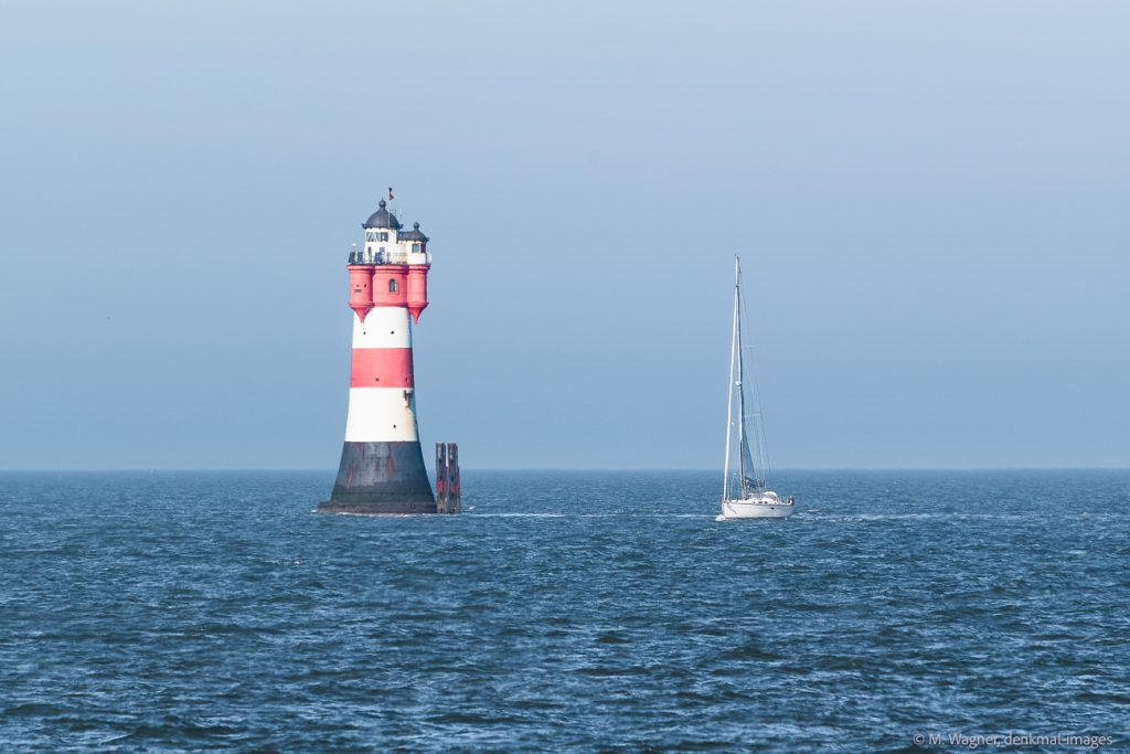 Leuchtturm Roter Sand im Meer vor blauem Himmel mit vorbeifahrendem Segelboot - Denkmalfotografie